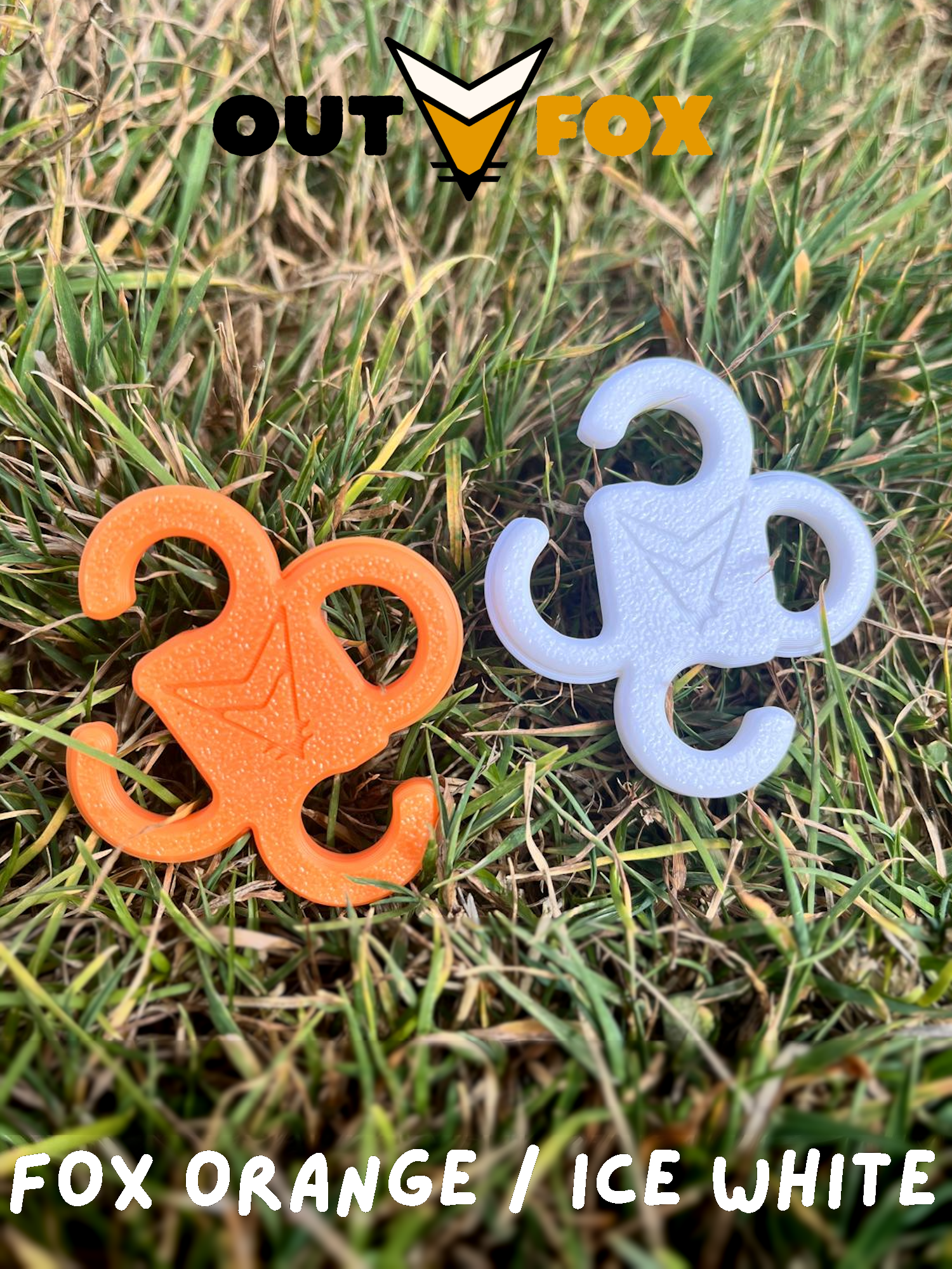 Two plastic guy line hooks, one Fox Orange and one Ice White, on grass with Outfox branding.